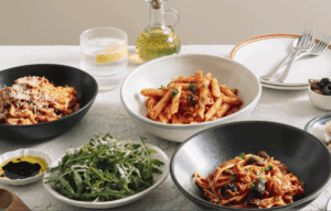 A table laid with bowls filled with different types of pasta: spaghetti primavera, penne amatriciana, beef ravioli bolognese and rocket salad.