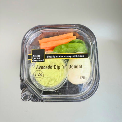 Packed snack container, including a hard boiled egg, carrot sticks, spinach leaves and avocado dip