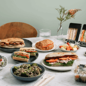 A table laid with a range of different 'Grab & Go' products, including a chicken schnitzel focaccia, chicken & salad baguette, soba noodle salad, fruit salad and tomato & cheese croissant.