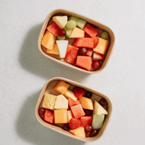 Two containers filled with chopped fruit including pineapple, watermelon, cantaloupe and grapes.